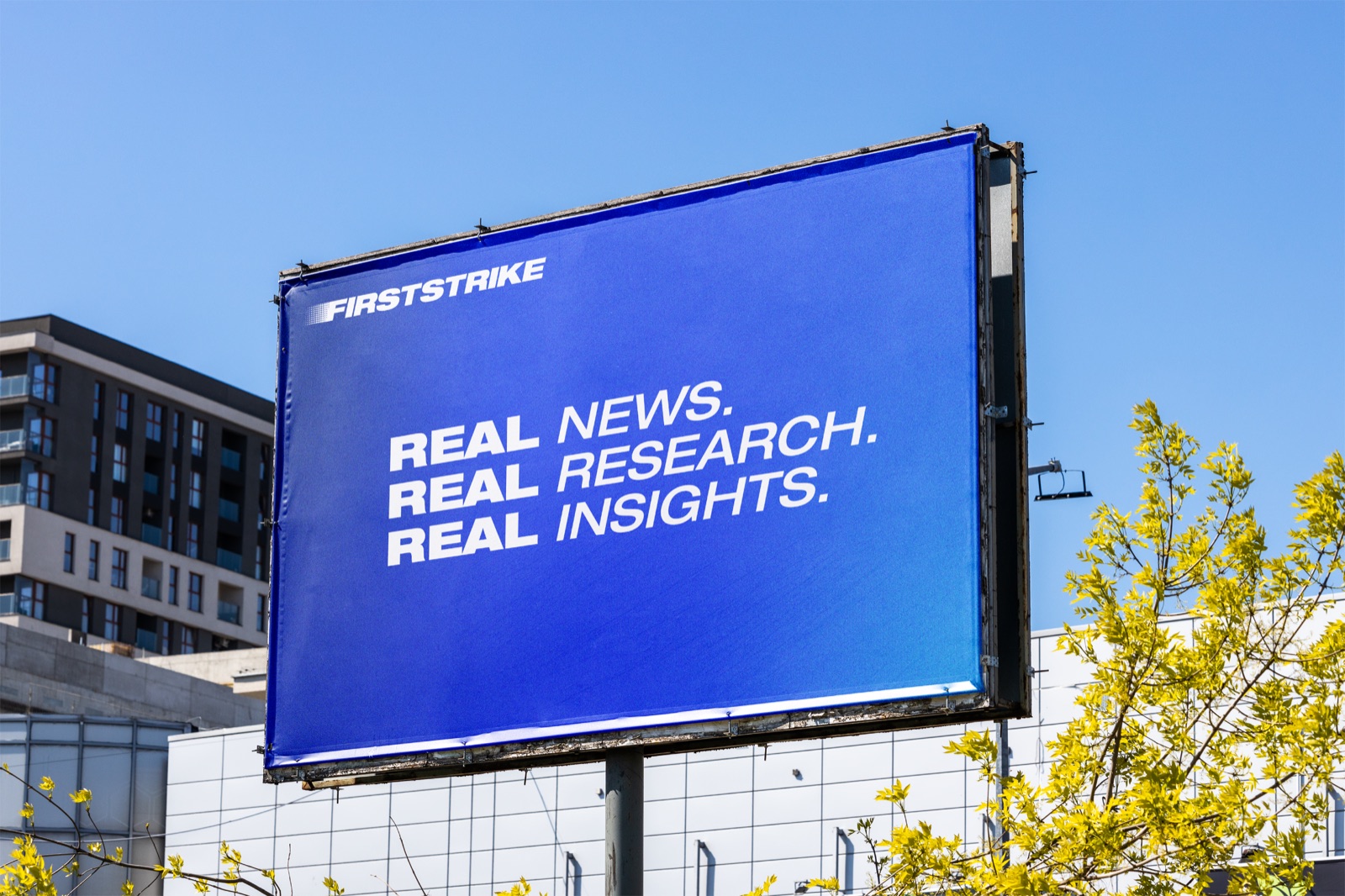 A billboard mockup reading Real News. Real Research. Real Insights. in blue and white above a city street